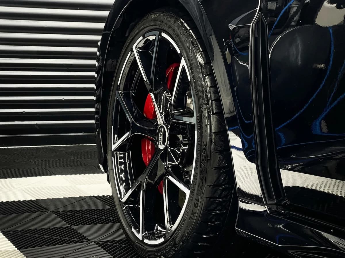 Plan serré sur la roue avant d'une Audi RS3, jante noire multibranche et étrier de frein rouge sous les LEDs du studio