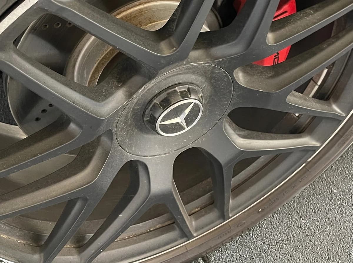 Macro sur une jante AMG noir mat encore encrassée, étoile centrale et étrier de frein rouge visibles