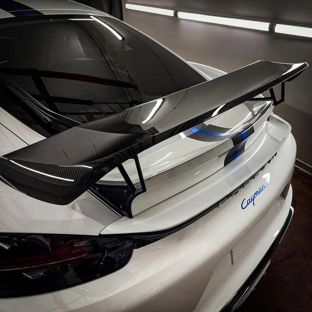 Vue arrière serrée d'une Porsche 718 Cayman T blanche, aileron carbone et bande bleue centrale