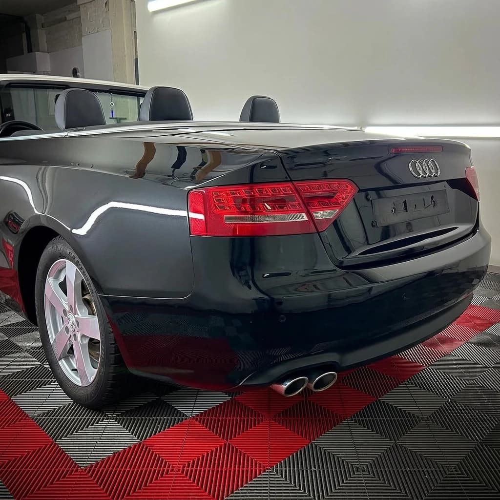 Plan serré sur l'arrière d'une Audi A5 Cabriolet noire capote baissée, feux et double sortie d'échappement chromée