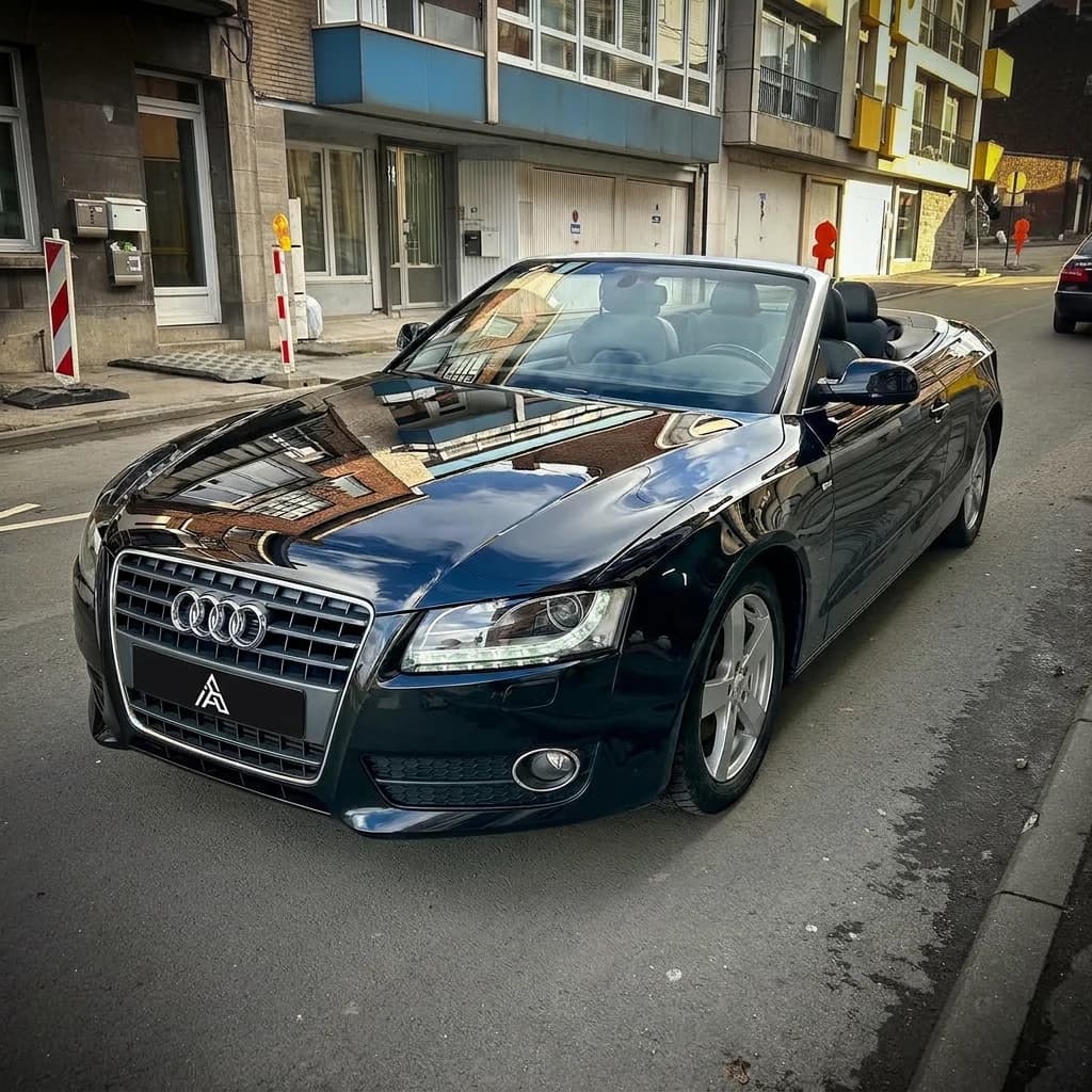 Audi A5 Cabriolet noire capote baissée, de trois quarts avant dans une rue commerçante