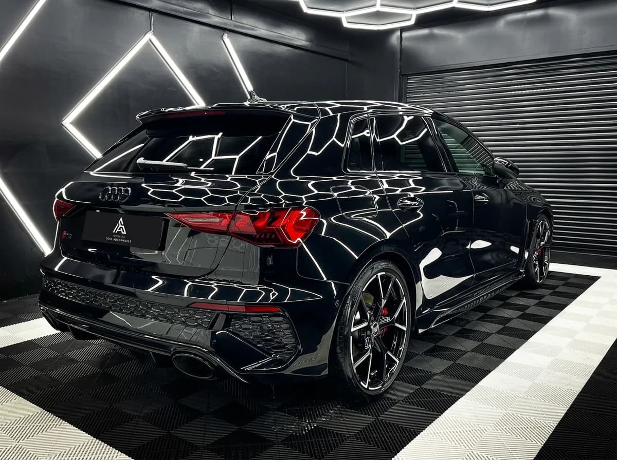 Audi RS3 noire de trois quarts arrière dans le studio de detailing, LEDs hexagonales réfléchies sur le flanc