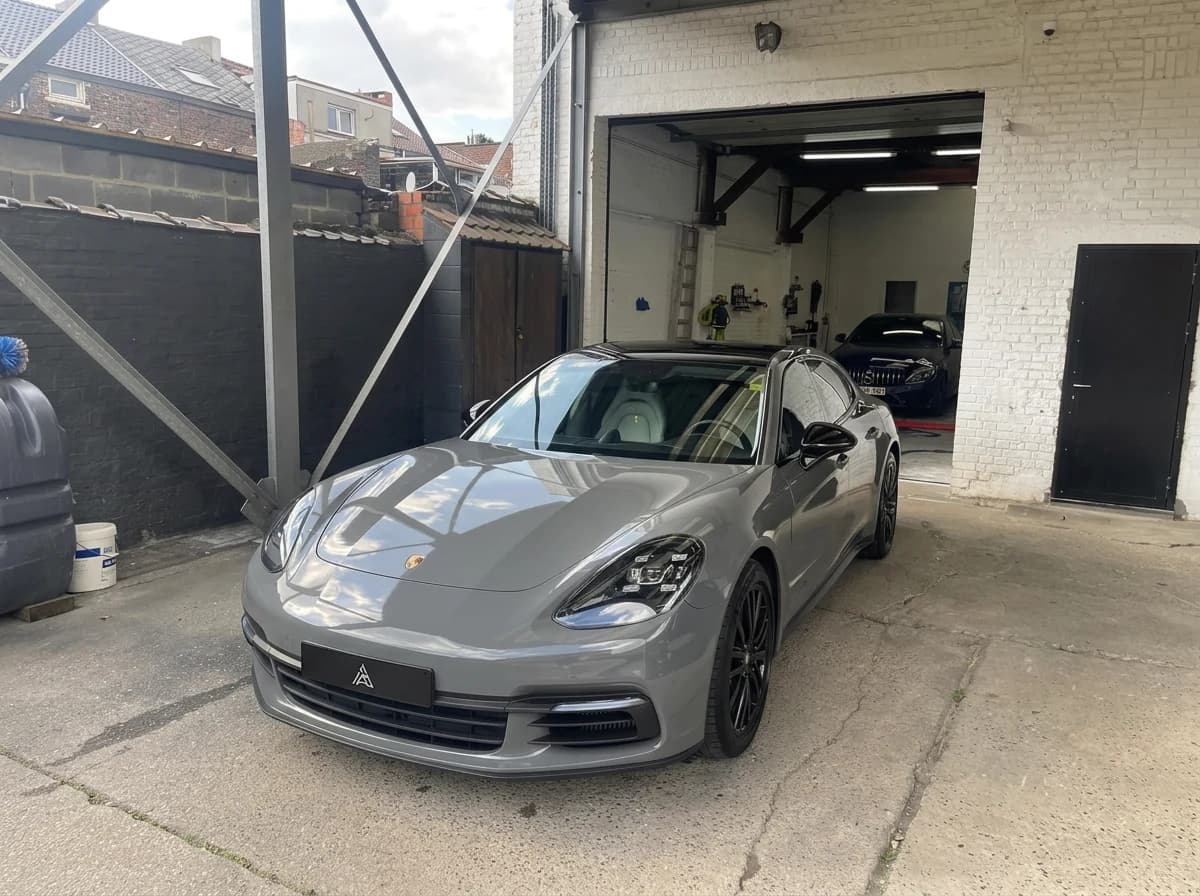 Porsche Panamera grise vue de face devant le box de l'atelier, sous un ciel couvert