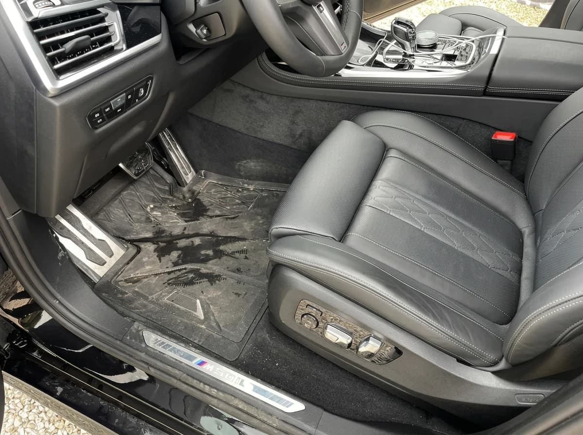 Place passager avant d'une BMW X7 pendant le shampoing : moquette mouillée et tachée, seuil de porte éclairé