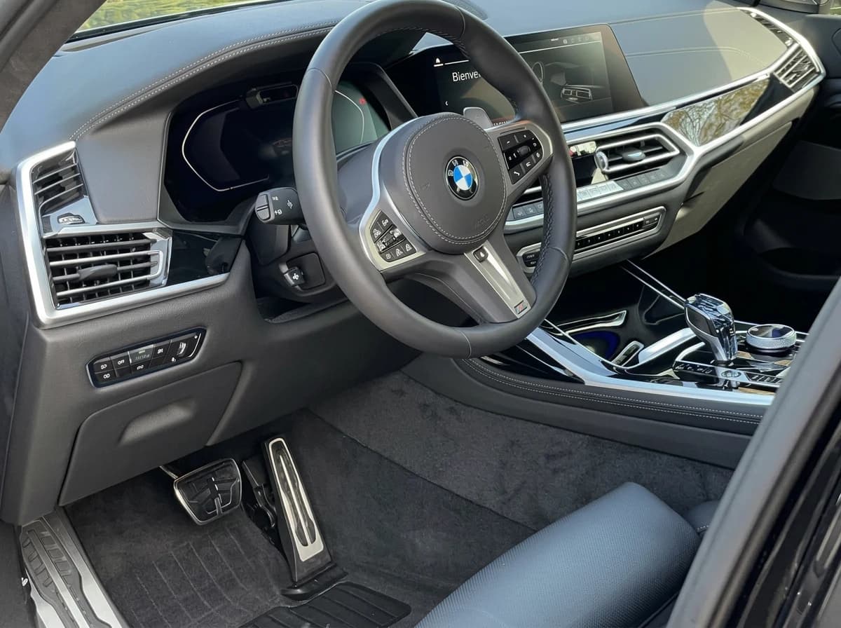Poste de conduite d'une BMW X7 côté conducteur : volant M, compteur numérique et pédales en inox