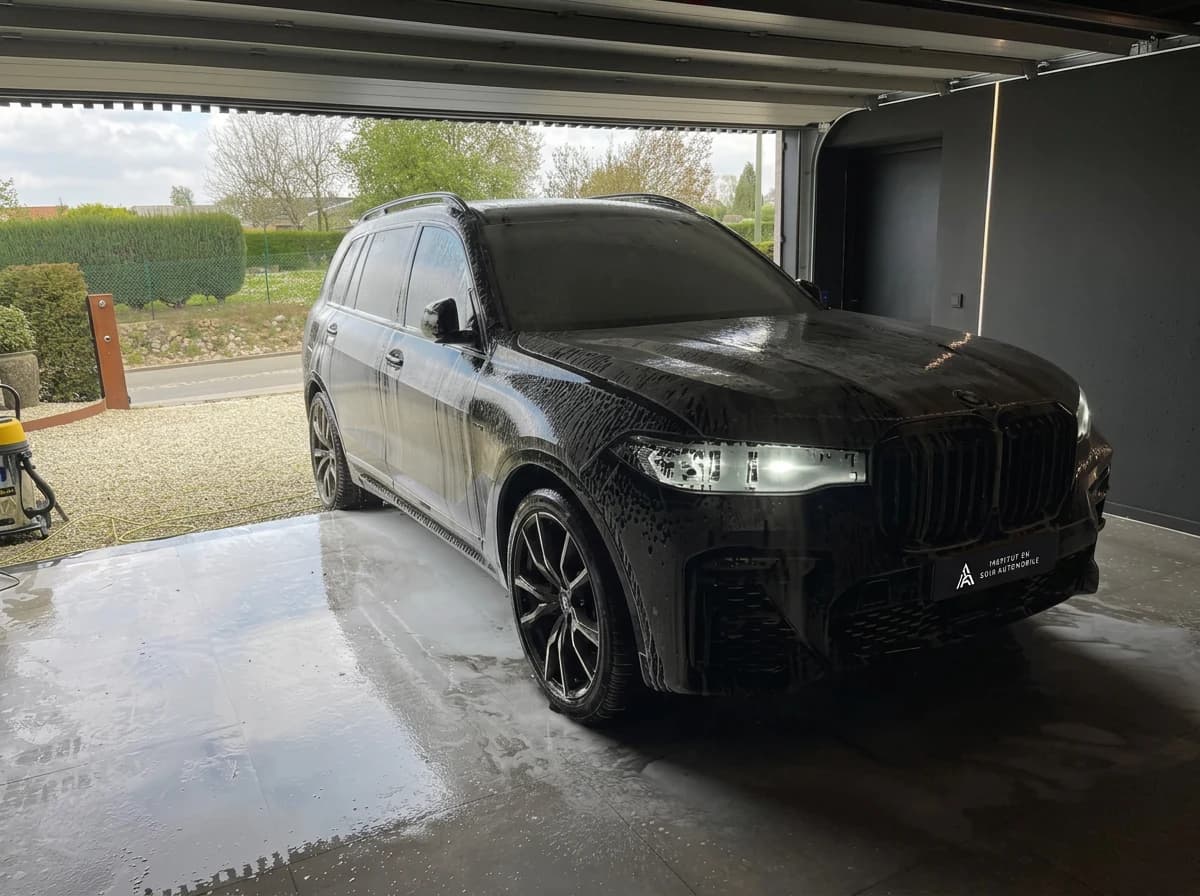 BMW X7 noire mouillée dans le box de lavage, feux allumés et sol en béton ruisselant