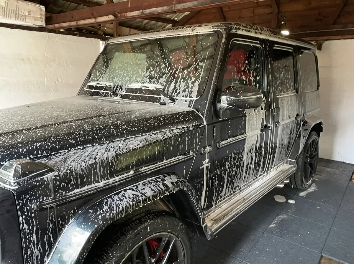 Mercedes-AMG G63 noir couvert de mousse active dans l'atelier, vu de trois quarts avant