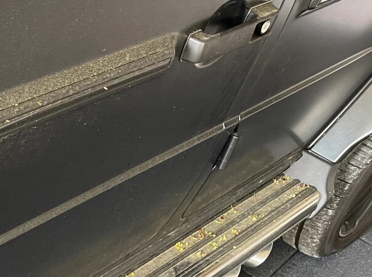 Vue basse le long du flanc d'une Mercedes-AMG G63 noir mat, marchepied couvert de pollen