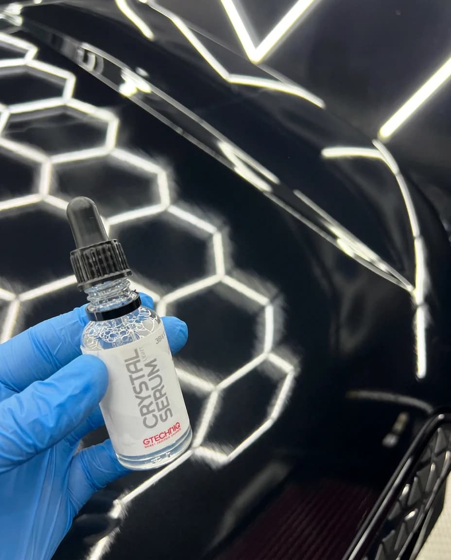 Flacon de revêtement céramique GTechniq Crystal Serum tenu par une main gantée de nitrile bleu, au-dessus d'un capot noir