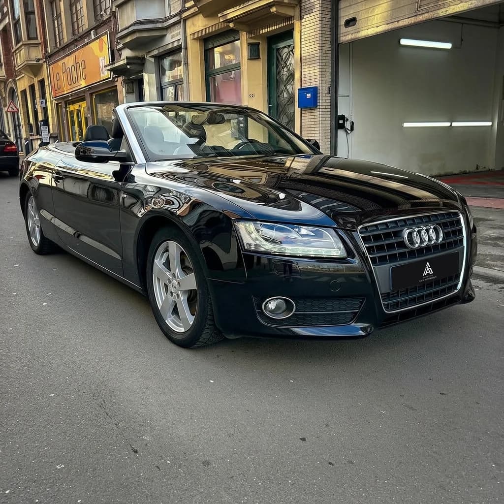 Audi A5 Cabriolet noire capote baissée, de trois quarts avant devant l'atelier
