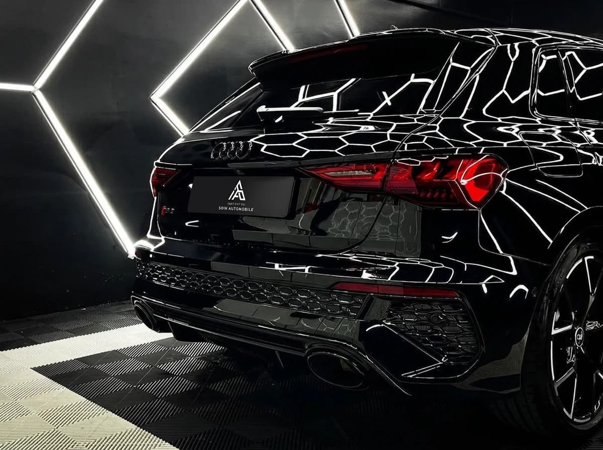 Plan serré sur l'arrière d'une Audi RS3 noire, feux et diffuseur sous l'éclairage du studio