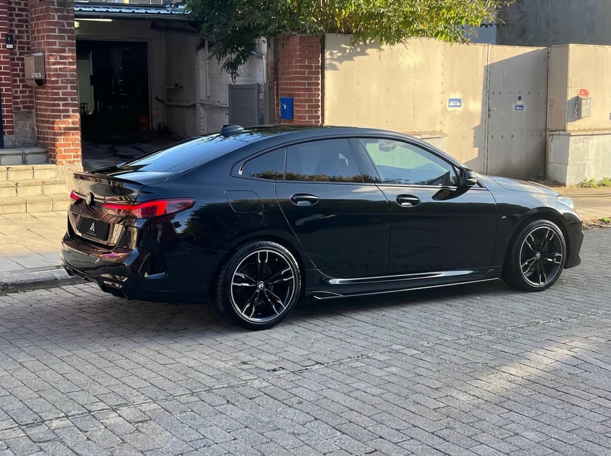 BMW Série 2 Gran Coupé noire vue de profil arrière dans une rue pavée, devant un bâtiment en brique