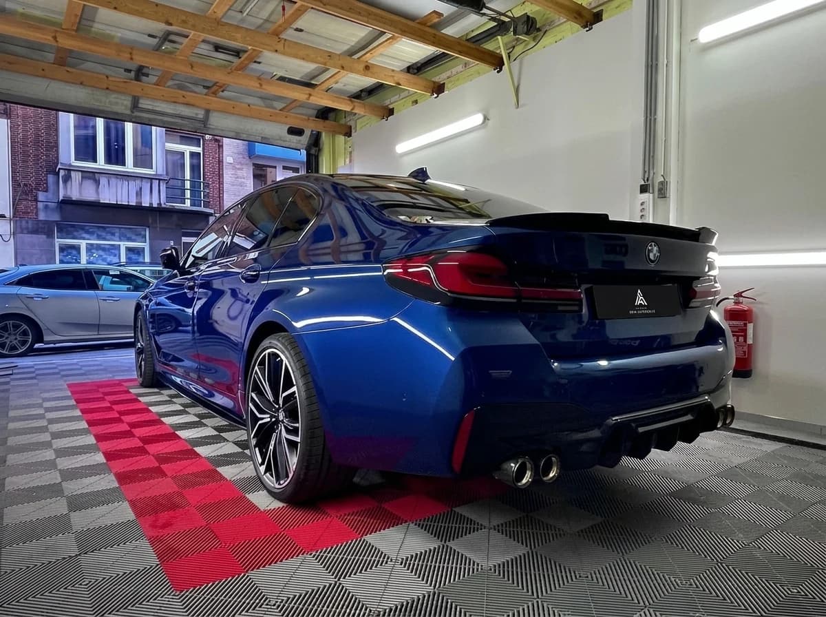BMW Série 5 hybride en teinte Phytonic Blue, de trois quarts arrière dans l'atelier sur le sol à damier rouge