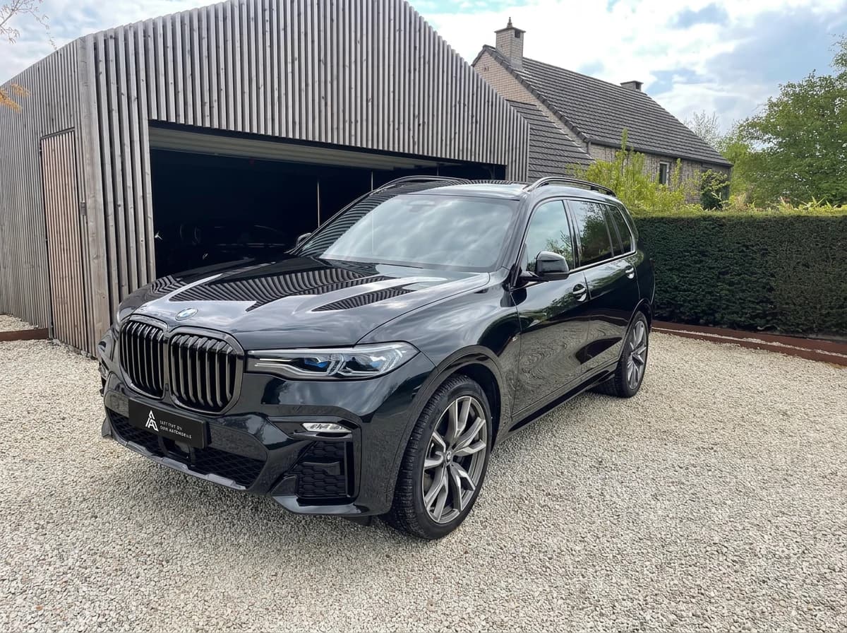 BMW X7 noire de trois quarts avant devant un hangar en bois