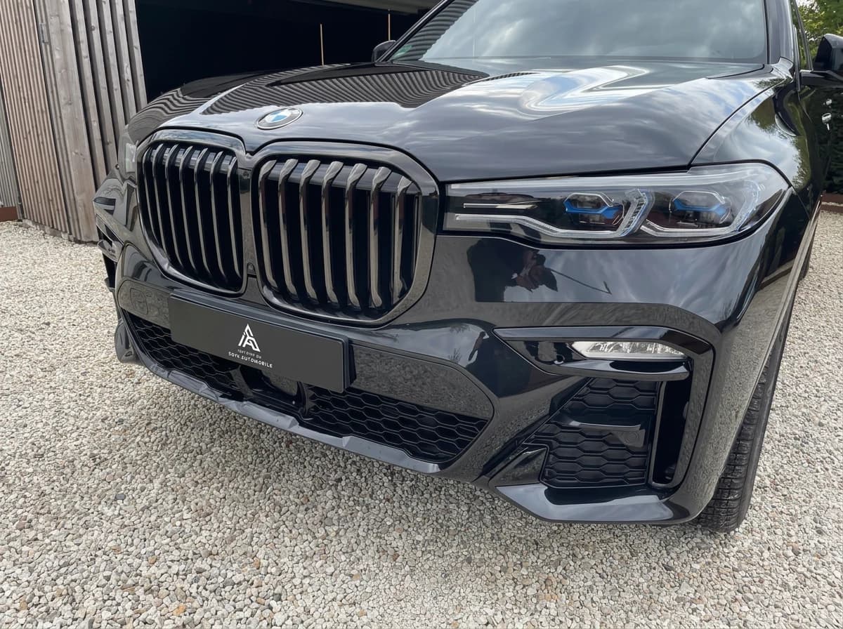 BMW X7 noire propre après lavage, de trois quarts avant dans une allée en graviers
