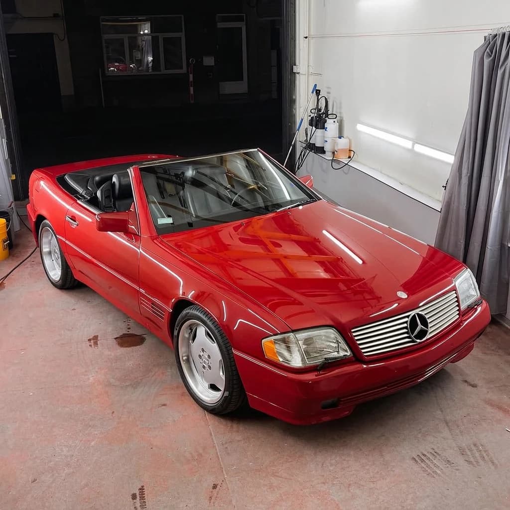 Mercedes 500 SL rouge capote baissée, de trois quarts avant dans l'atelier au sol béton rouge