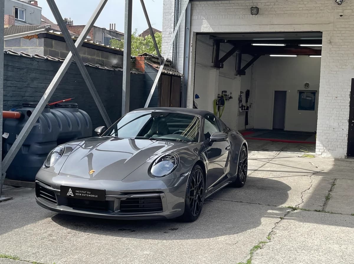Porsche 911 Targa 4S grise de trois quarts avant devant le box de l'atelier, sous un ciel couvert