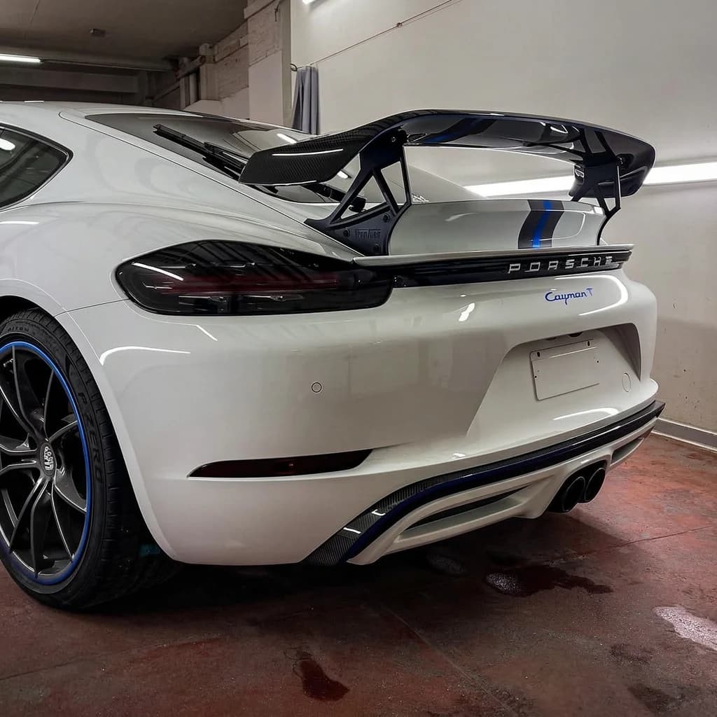 Porsche 718 Cayman T blanche de trois quarts arrière dans l'atelier, grand aileron carbone à fixation col de cygne