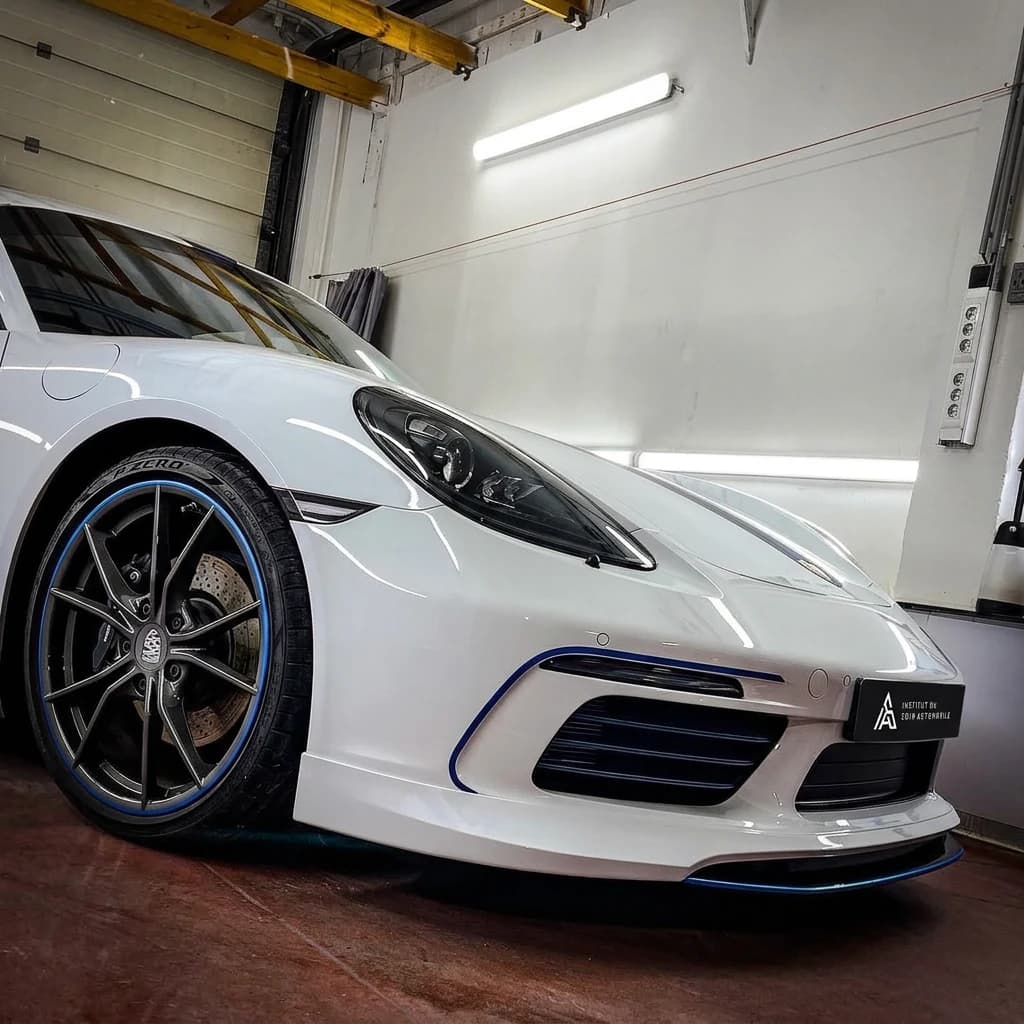 Porsche 718 Cayman T blanche à liserés bleus et aileron carbone, de trois quarts avant dans l'atelier