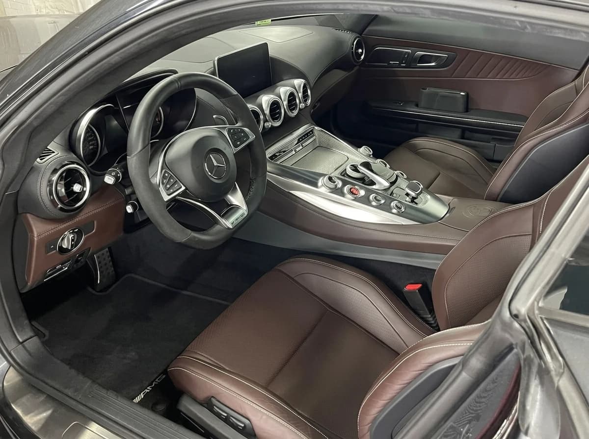 Vue large de l'habitacle d'une Mercedes-AMG GT par la portière passager : cuir brun, aérateurs ronds et console à boutons