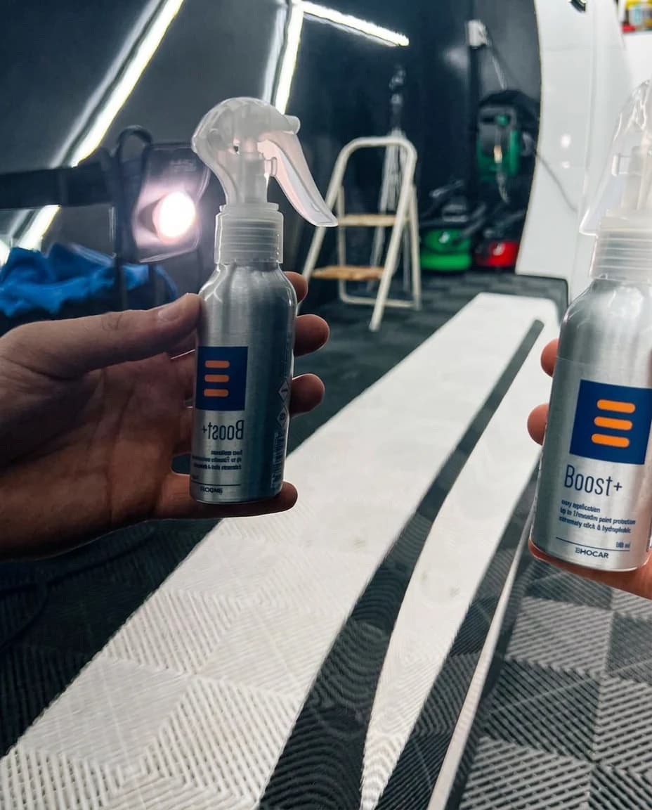 Deux flacons en aluminium Boost+ tenus en main dans l'atelier, LEDs et tapis de protection au sol